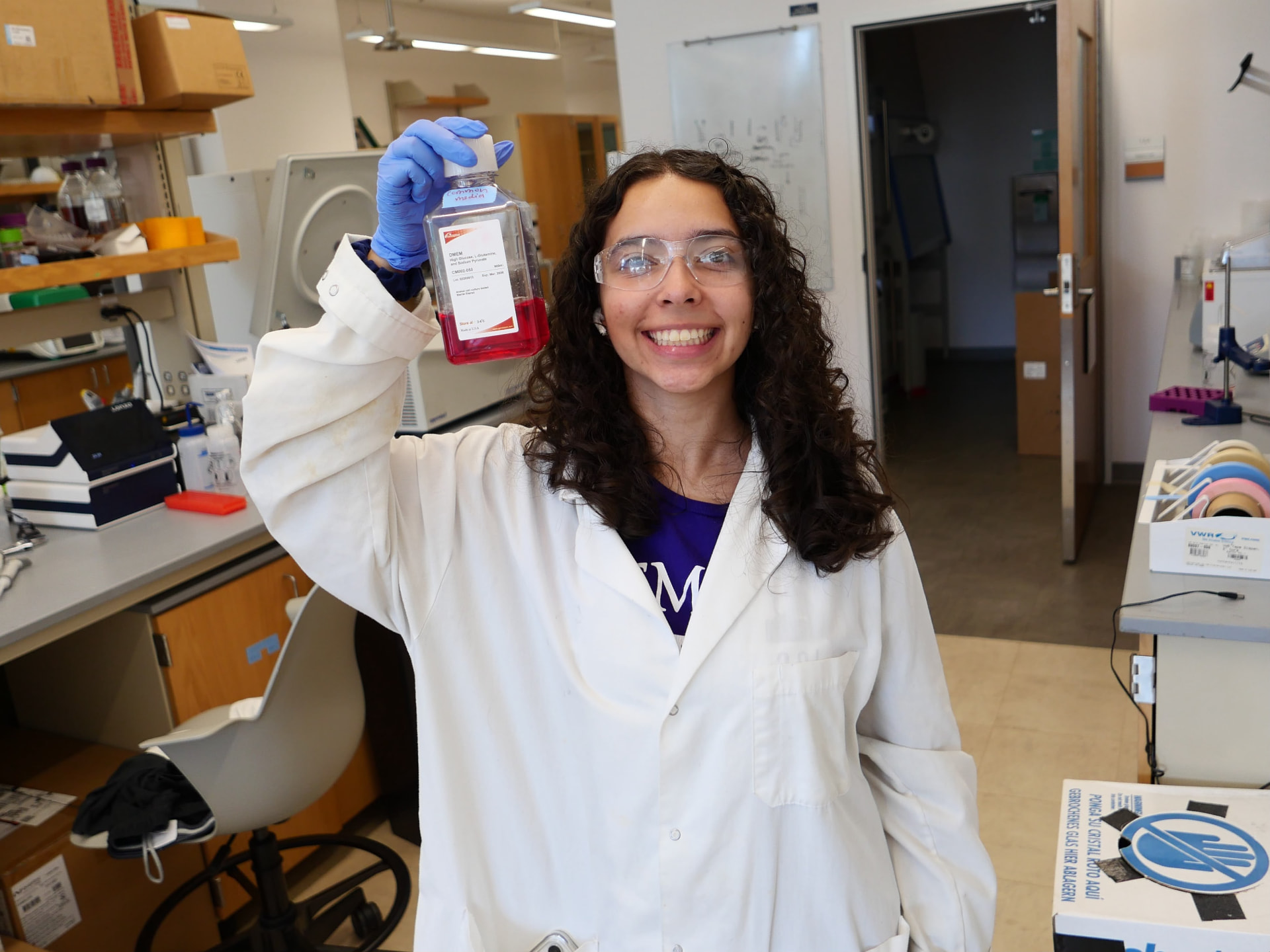 Dou Lab researcher holding a bottle of cell culture media at the bench